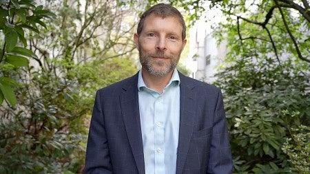 Chris poulsen wearing a blazer and collar shirt in front of a tree background