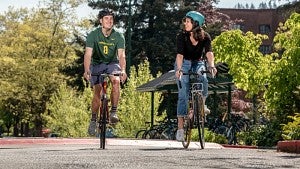 Two students riding bikes through UO's campus.