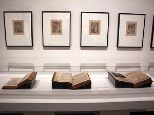 museum exhibit with framed works and books in glass case
