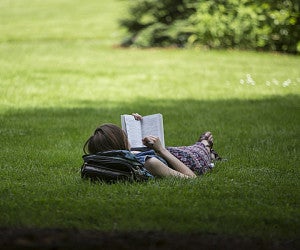 English Master's Degree (photo of student lying on grass reading a book)