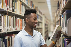 student smiling with book in hand in library