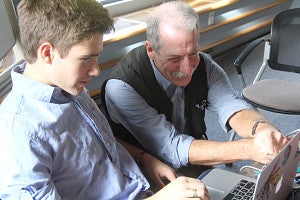 A professor helps a student on a laptop