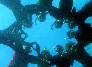 Students underwater in diving gear linking arms in circle while throwing the O