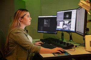 female researcher sitting at 3 computer screens