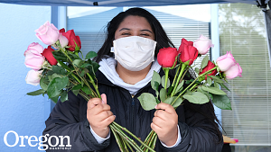 woman in facemask with smiling eyes holding two bouquets of roses