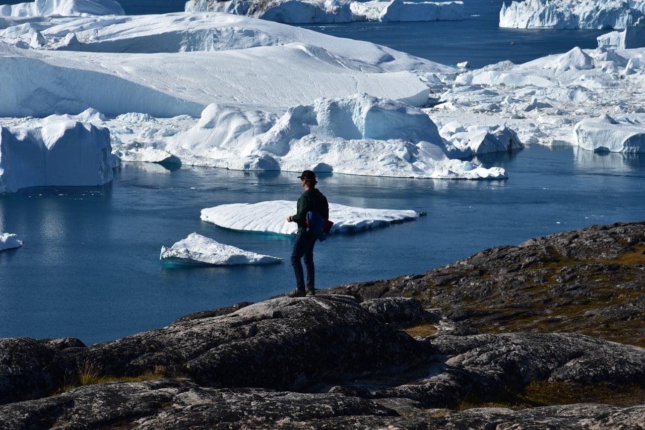 Man stands on edge of mountain looking at icebergs.