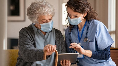 A nurse helps an older woman on an iPad 