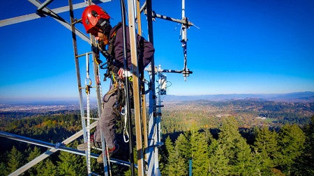 A climber, high up in a telecommunications tower on a South Eugene ridge
