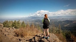 Student stands on rock overlooking Eugene from the top of a hike