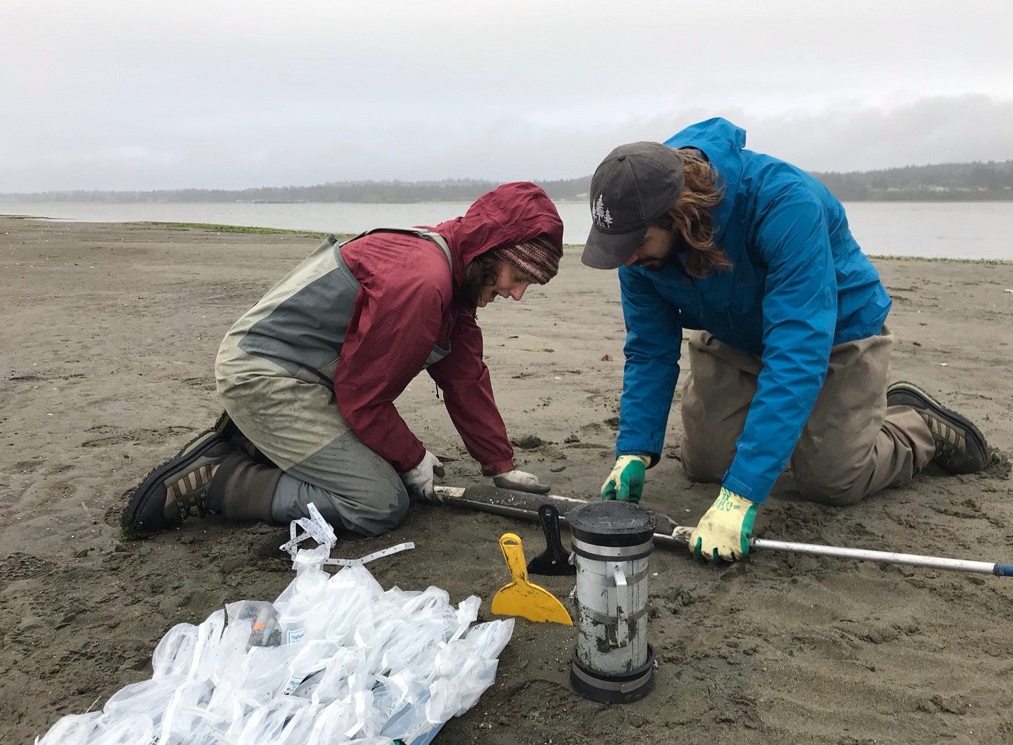 researchers examining sediment core on sandy coastal shore