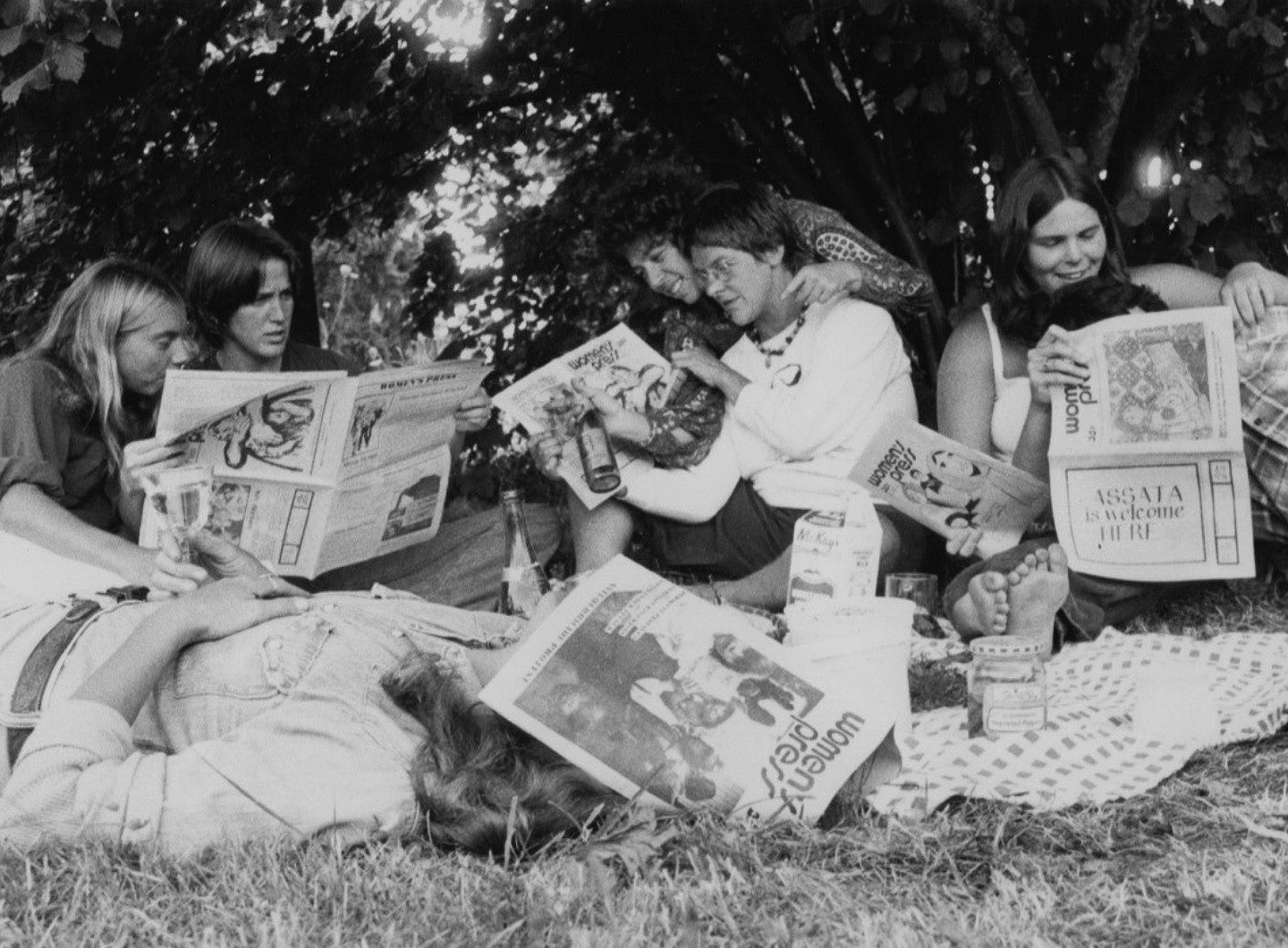 women lying together on grass reading Women's Press newspaper