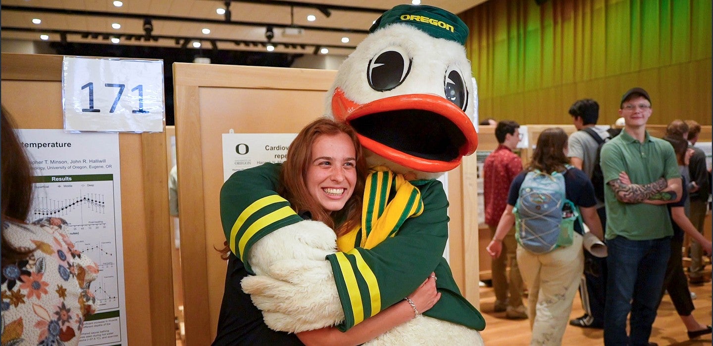 a student hugs the Oregon Duck at a research event