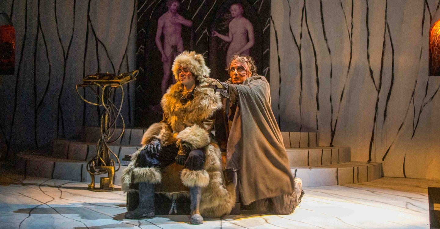 a stage production photo of Frankenstein with one person dressed in furs and another person dressed as a monster