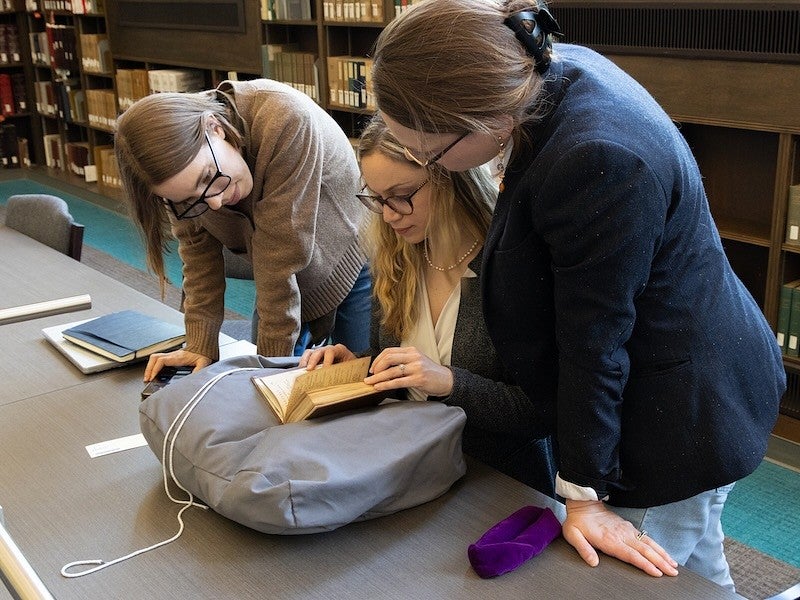 group of women looking at a book from an archive in the library