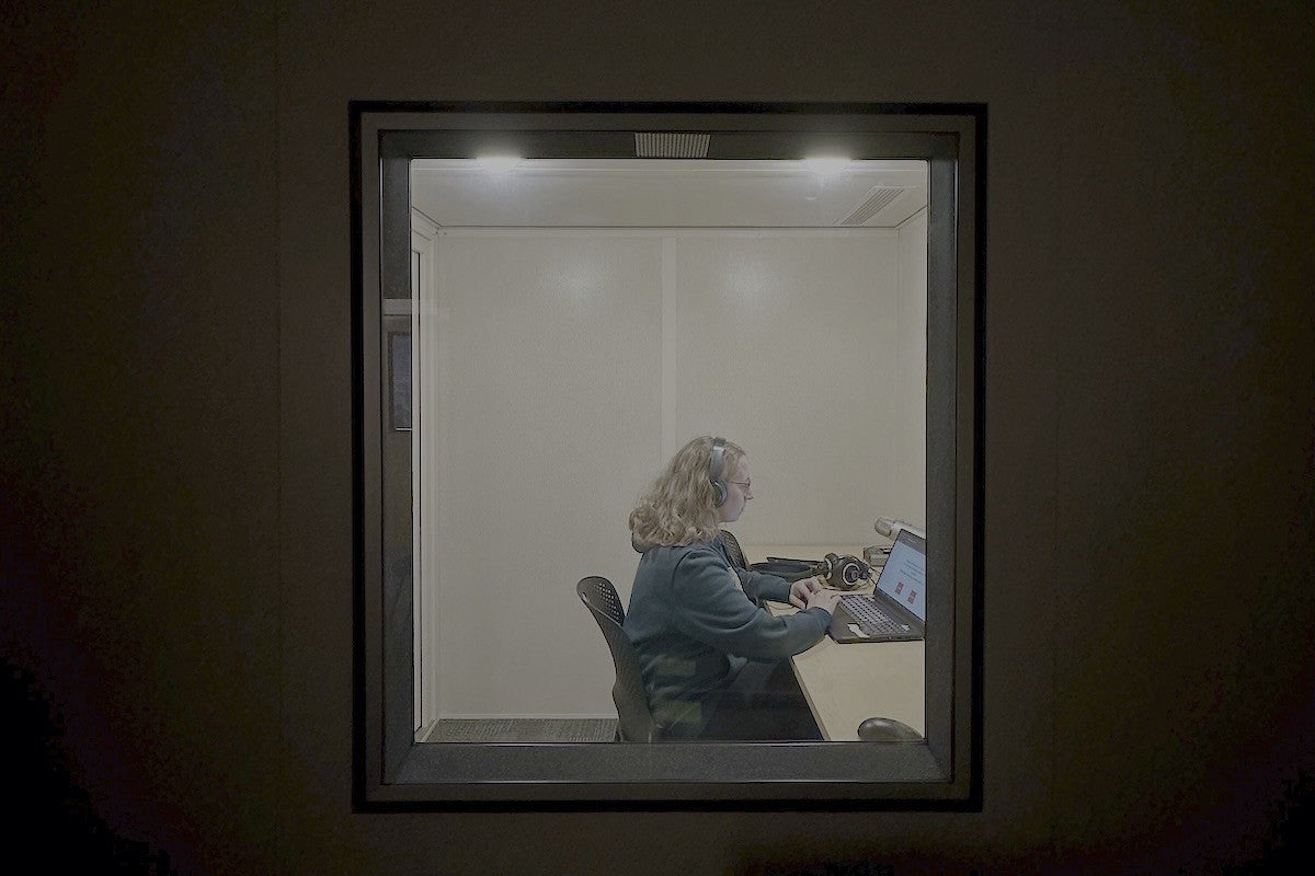 woman wearing headphones sitting in front of a computer in a sound booth