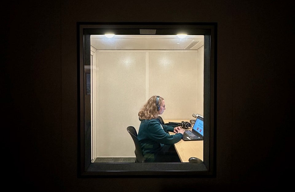 woman wearing headphones sitting in front of a computer in a sound booth