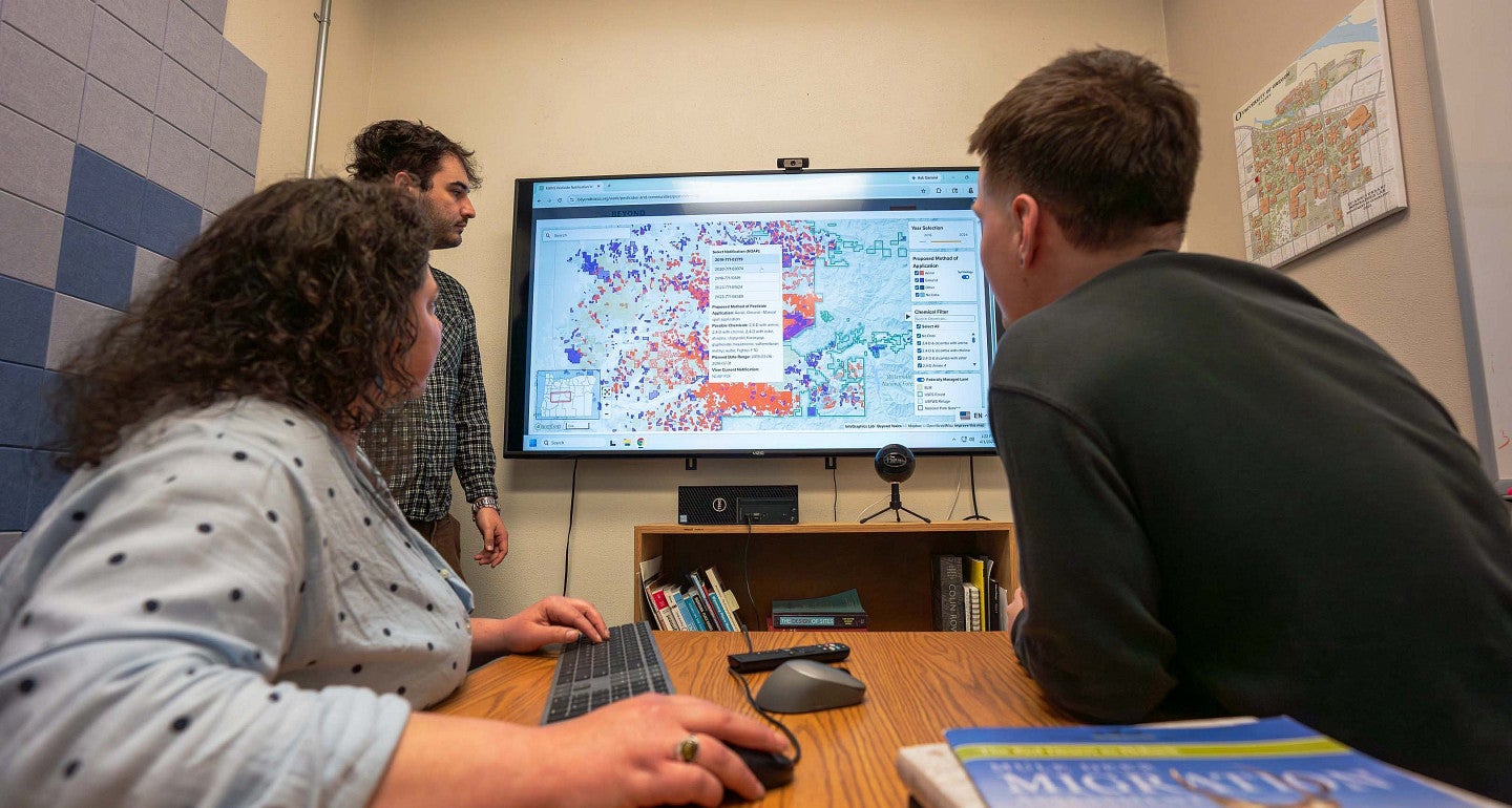 three people at a desk looking at a map on a screen