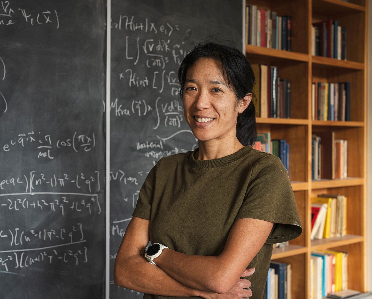 a person poses next to a chalkboard filled with equations 