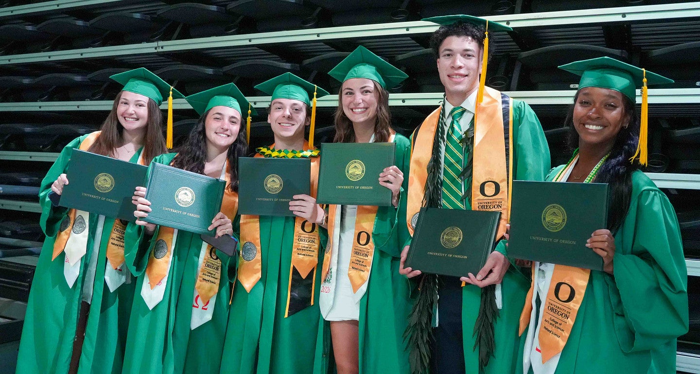 a group of people hold green diploma covers wearing green cap and gowns