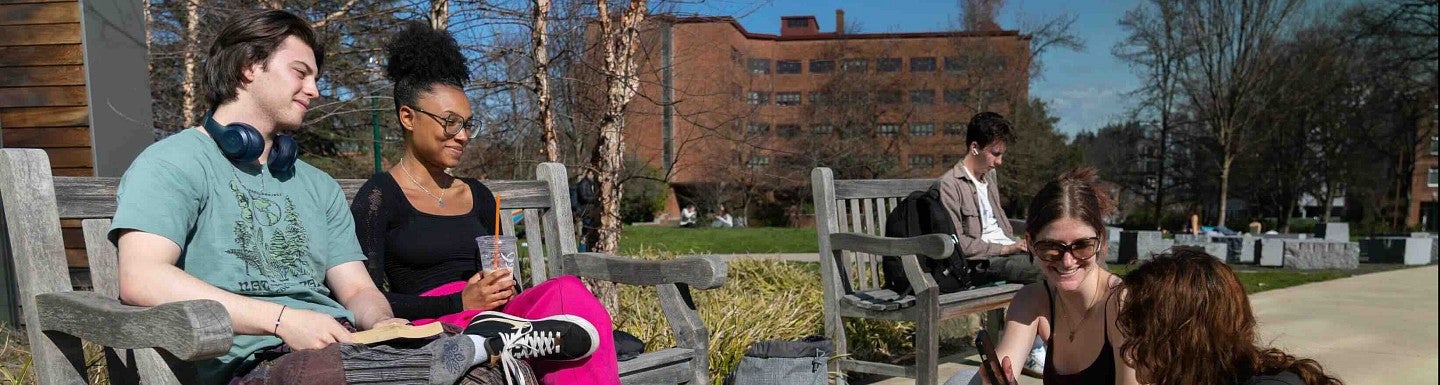 four students gathered, two on a bench, two sitting on the sidewalk