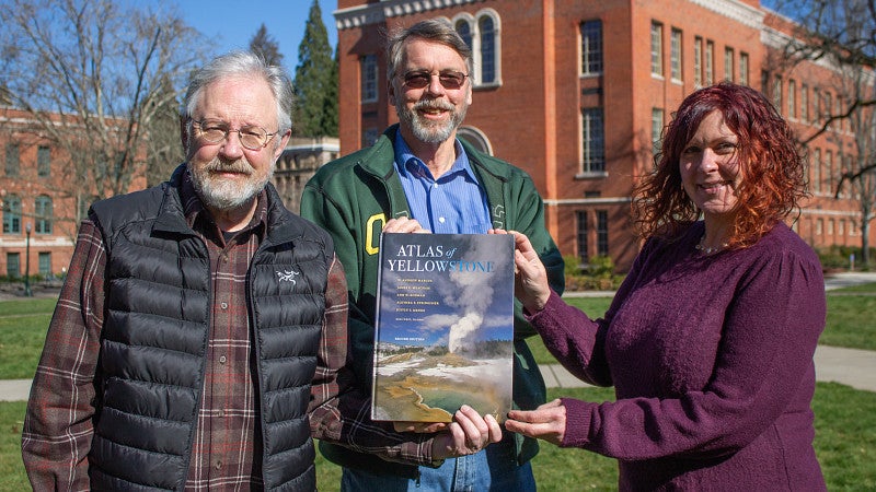 meacham, marcus and steingisser pose outside on UO campus holding atlas
