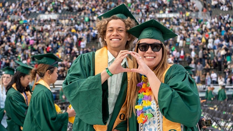 two grads make the UO logo with their hands