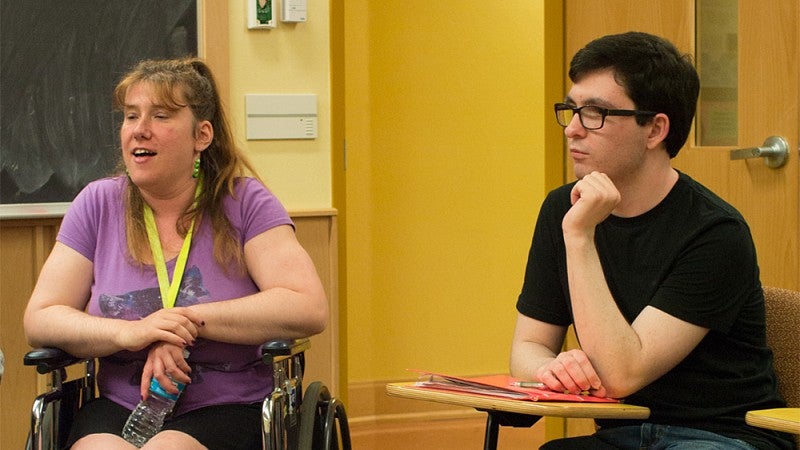 A person in a wheelchair and person sitting at a desk in classroom