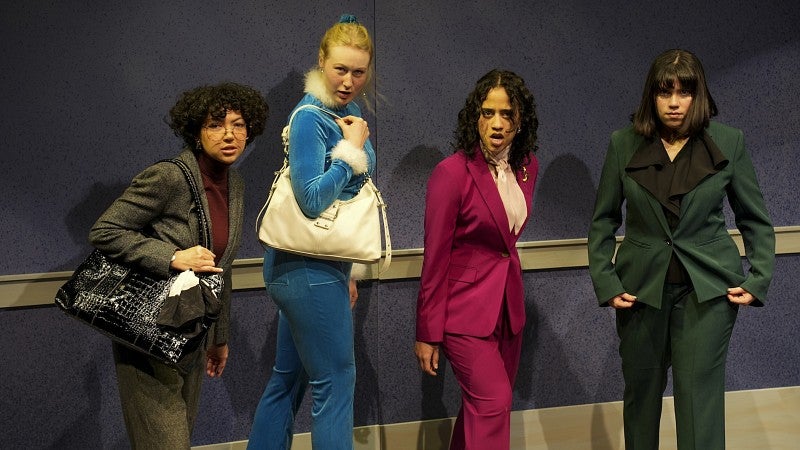 four women dressed in professional attire making dramatic tough faces