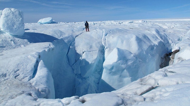 A researcher standing next to a large crevasse in the ice sheet