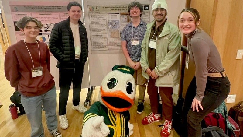 Students gathered around a research project with the duck mascot