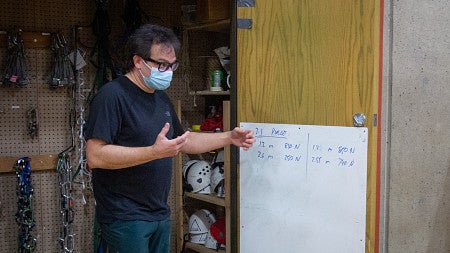 Physics Professor Graham Kribs and students in the Science of Climbing course measure the load on a climbing rope and pulley configuration using a force meter and a bundle of tires for weight. 