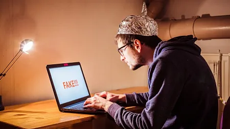 a conspiracy theorist in a foil hat typing on a laptop
