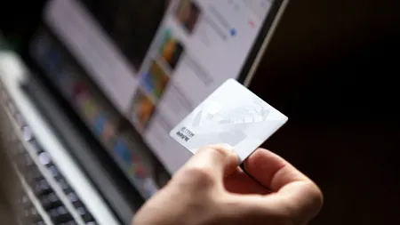 a hand holding a credit card in front of a computer screen