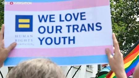 a protester holding up a sign in support of trans youth