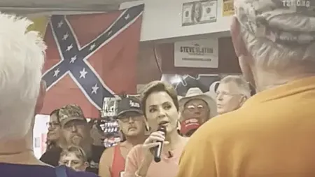 a candidate for US senator stands in front of a Confederate flag
