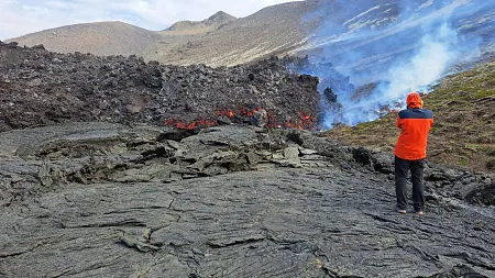 a person wearing orange stands near a lava flow
