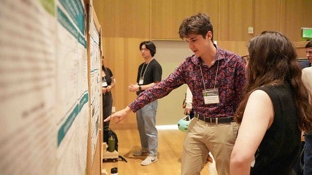 a student points to his poster while talking with another person