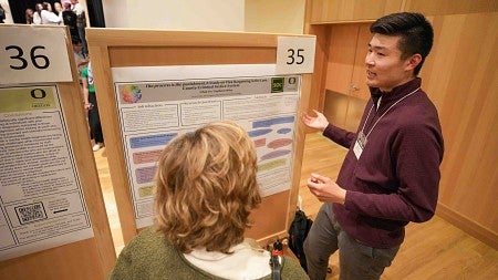 a student wearing a red sweater shares his research with a person