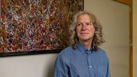 a man with shoulder length gray-ish hair stands next to a Jackson Pollock painting