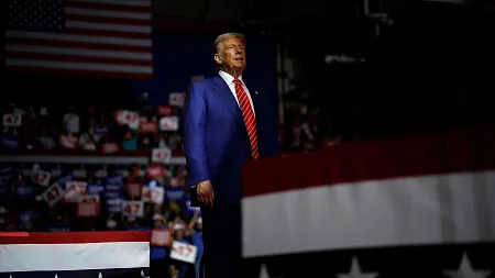 donald trump wearing a blue suit and red tie, shrouded by shadows