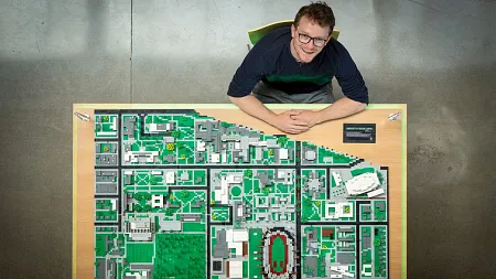 a person sits at a table with a Lego UO campus nearby