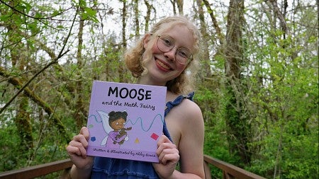 a student holds her book with a background of trees