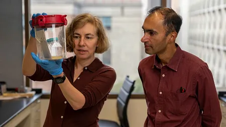 two people in a lab setting, person on the left holding a cylinder as a person on the right looks at it