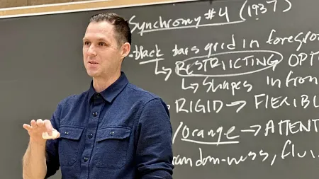 Colin Williamson stands in front of a blackboard, lecturing a class