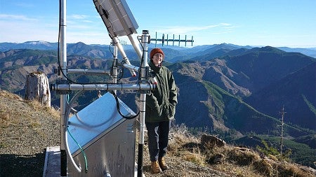 A person standing next to an antenna on a mountain