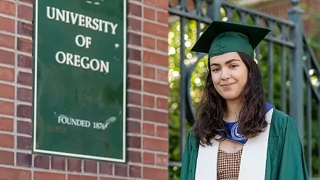 a person wearing a cap and gown by dad's gate at the UO campus