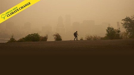A person walking across a ridgeline with a city skyline in the background obscured by wildfire smoke