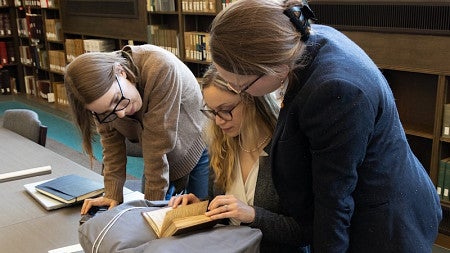 group of women looking at a book from an archive in the library