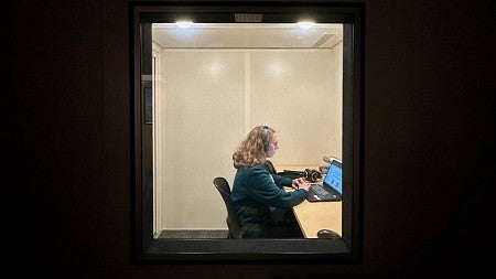 woman wearing headphones sitting in front of a computer in a sound booth