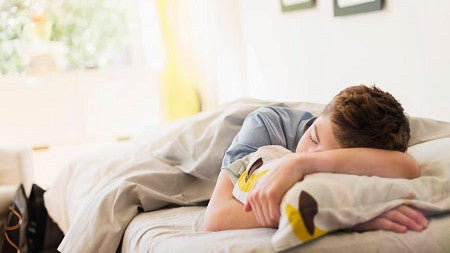 a teenager sleeping on a bed beside a sunny window